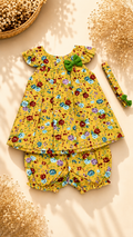 A baby girl's two-piece outfit set consisting of a yellow floral romper and matching bloomers, styled with a matching headband on a beige background with dried floral props.
