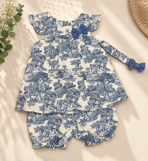 A baby girl's two-piece clothing set featuring a long-sleeve top and matching shorts in a blue and white toile de Jouy pattern, styled flat-lay on a beige background with decorative greenery.