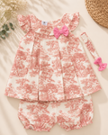 A baby girl's three-piece outfit set featuring a ruffled sleeveless top, matching bloomers, and a headband, all in a pink and white toile de Jouy pattern with a pink bow accent, laid flat on a beige background.