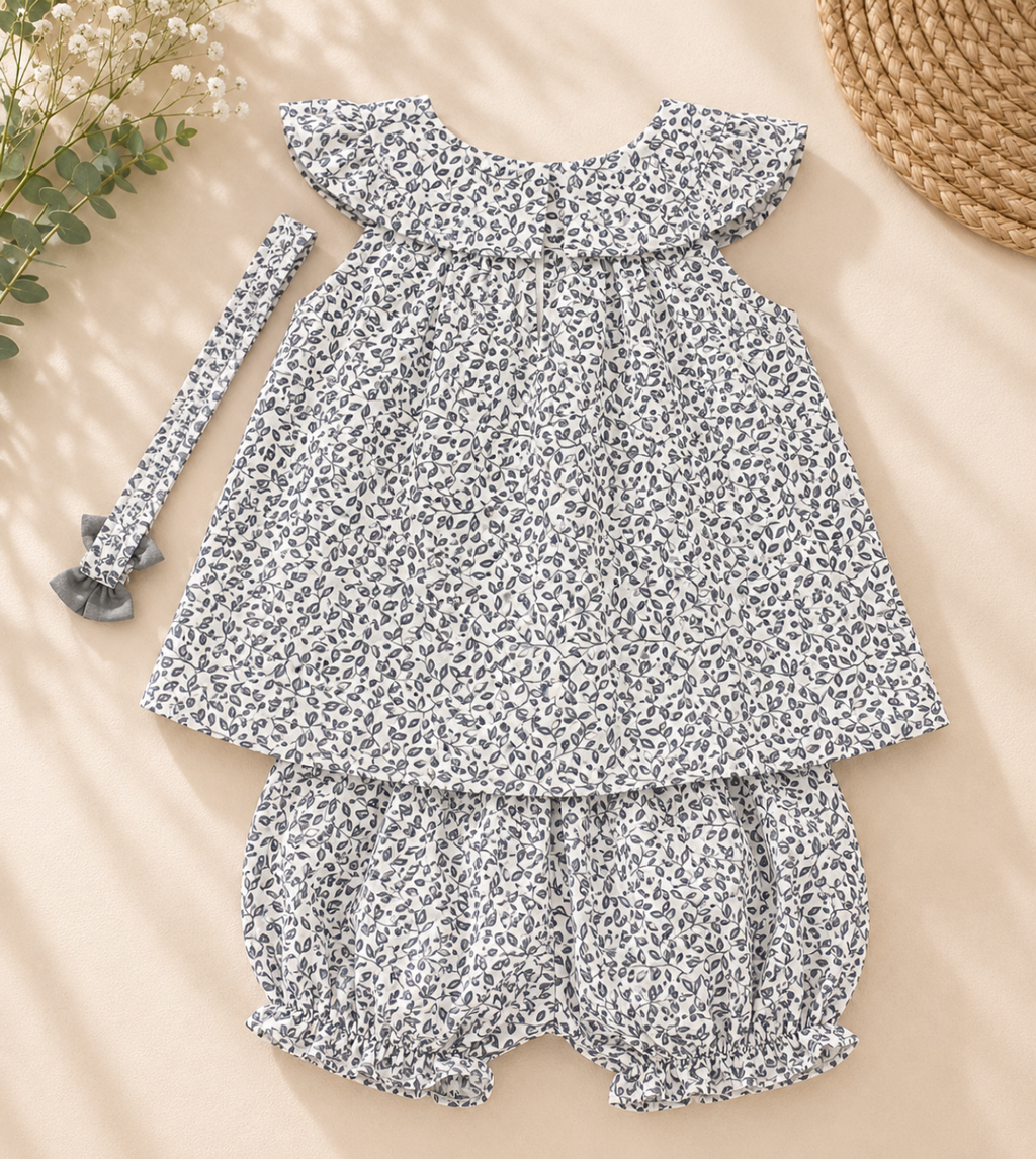 A baby girl's two-piece outfit set featuring a short-sleeve ruffle-sleeve top and matching ruffled bloomers, both in a black and white leopard print, laid flat on a beige background with a matching headband and decorative props.